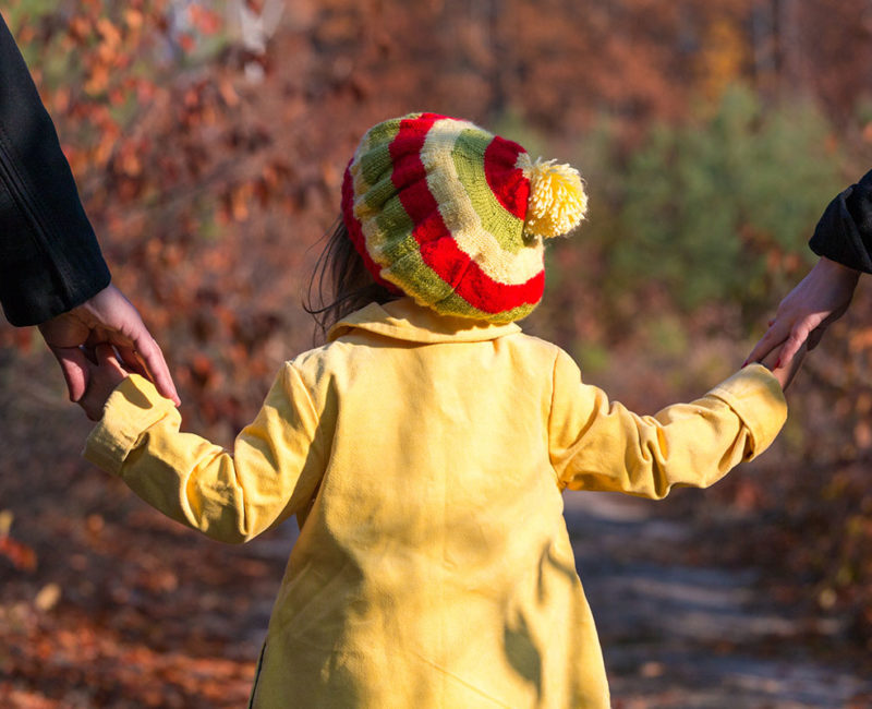 child in yellow jacket walks holding her parents' hands