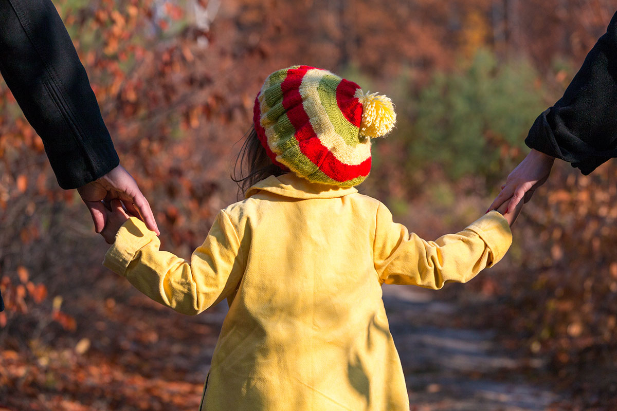 child in yellow jacket walks holding her parents' hands