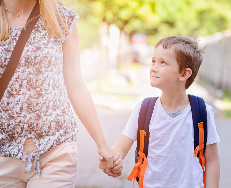 boy holds his mother's hand as they walk to school together