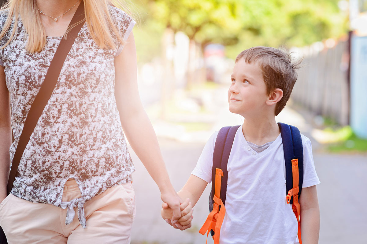 boy holds his mother's hand as they walk to school together