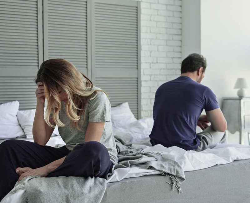 divorced couple sits on opposite ends of bed facing away from each other