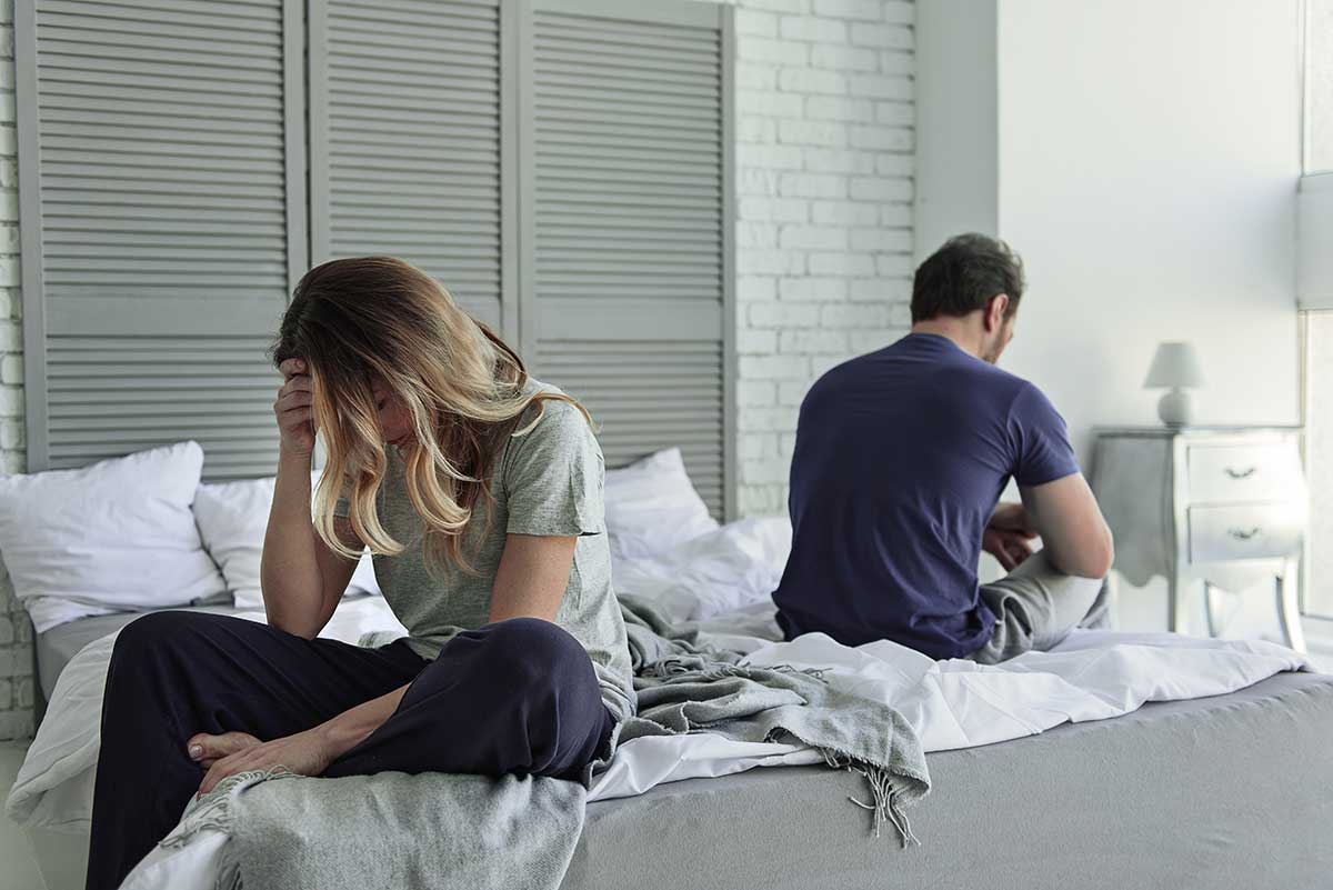 divorced couple sits on opposite ends of bed facing away from each other