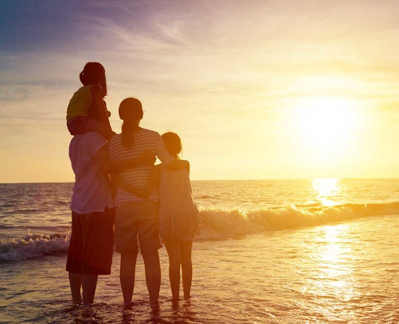 family stands close hugging each other on the beach at sunset