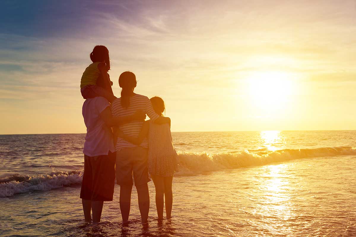 family stands close hugging each other on the beach at sunset