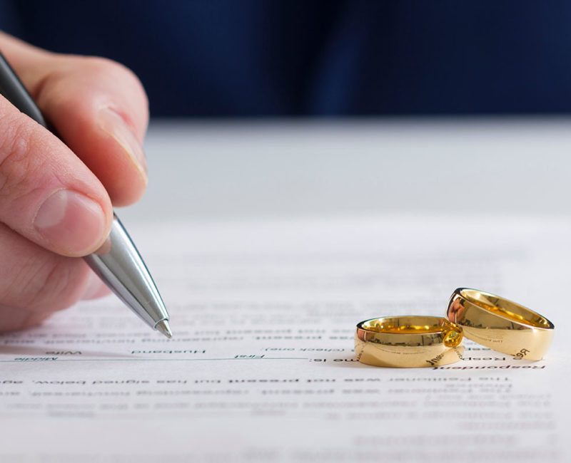 wedding wings sit on top of divorce papers as a man gets ready to sign