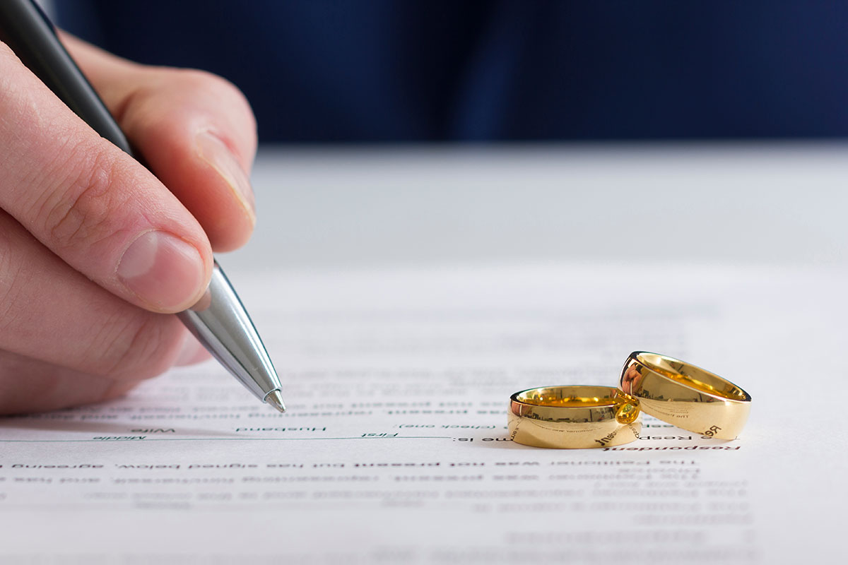 wedding wings sit on top of divorce papers as a man gets ready to sign