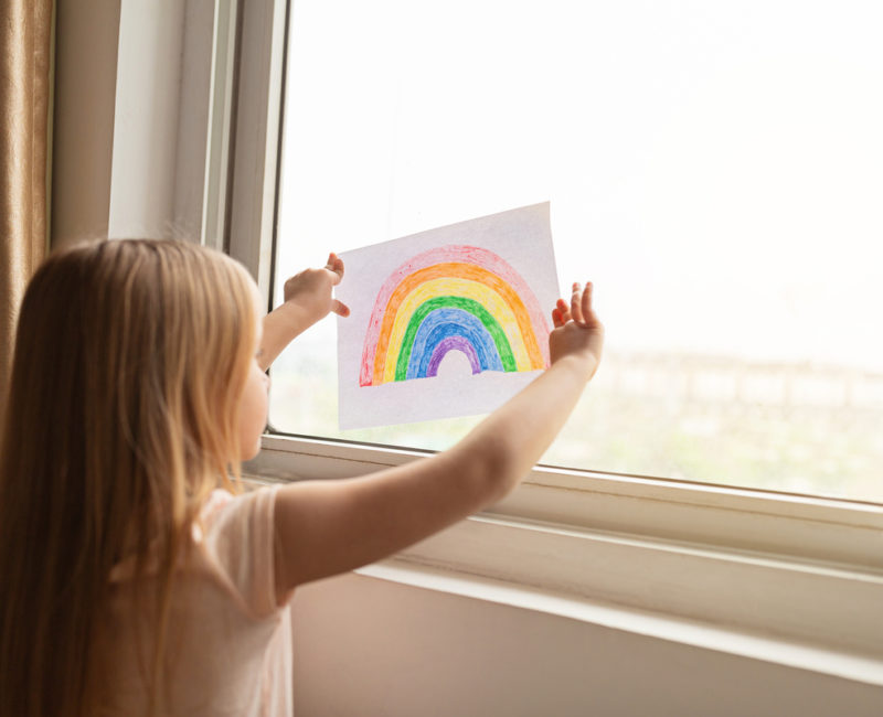 Child hangs a picture of a rainbow on a window