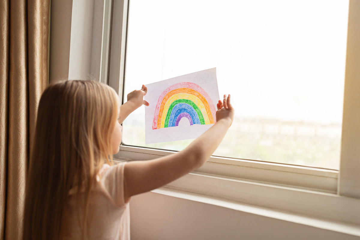 Child hangs a picture of a rainbow on a window