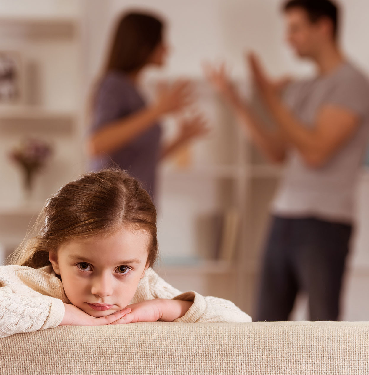 Child sitting on a couch as parents argue in the background