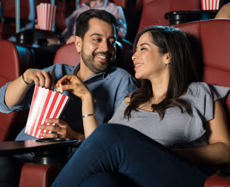 Married couple sitting at a movie theater eating popcorn